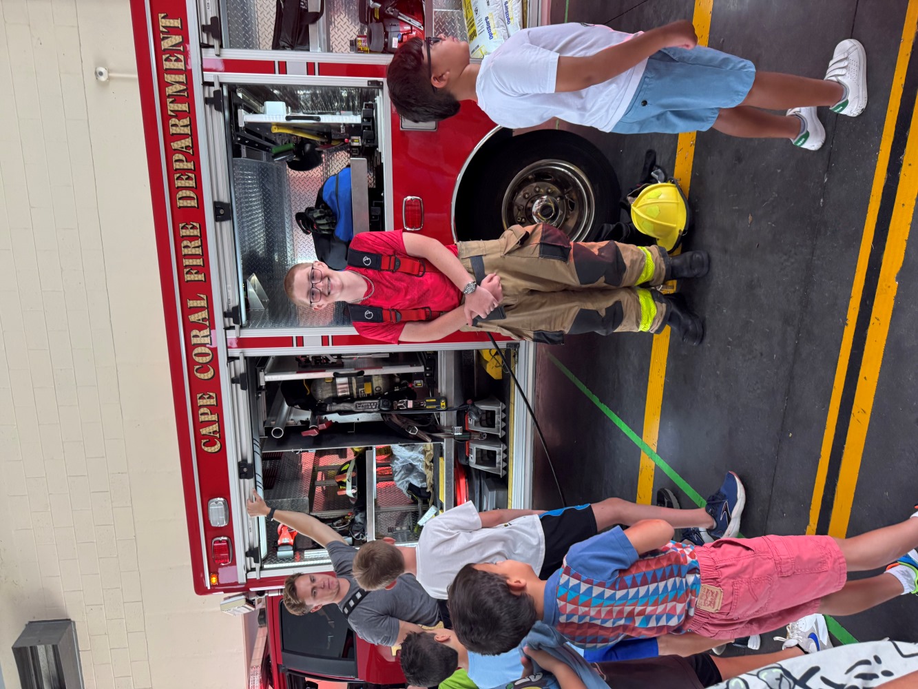 Firefighter stands by an open Cape Coral fire engine while children listen during a station tour.